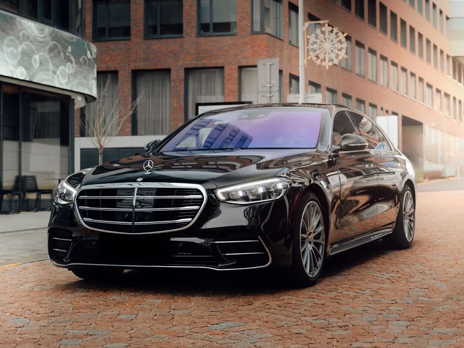 Black Mercedes-Benz S-Class on a cobblestone street between brick buildings